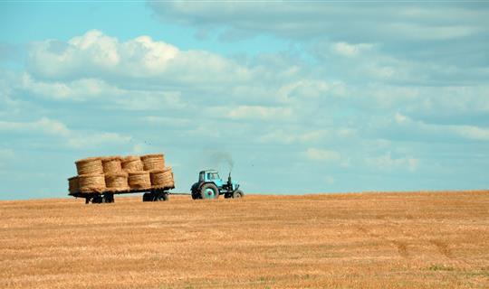 a tractor on a field pulling a trailer of hay