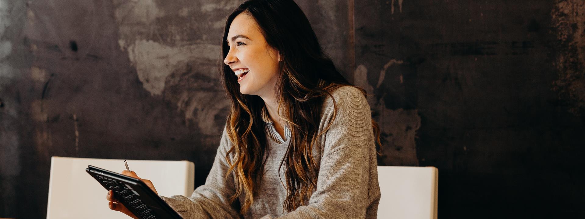 a lady sat at a table smiling and holding a tablet