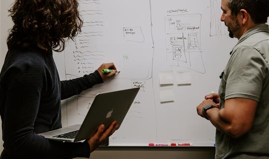 two people studying plans on a wall